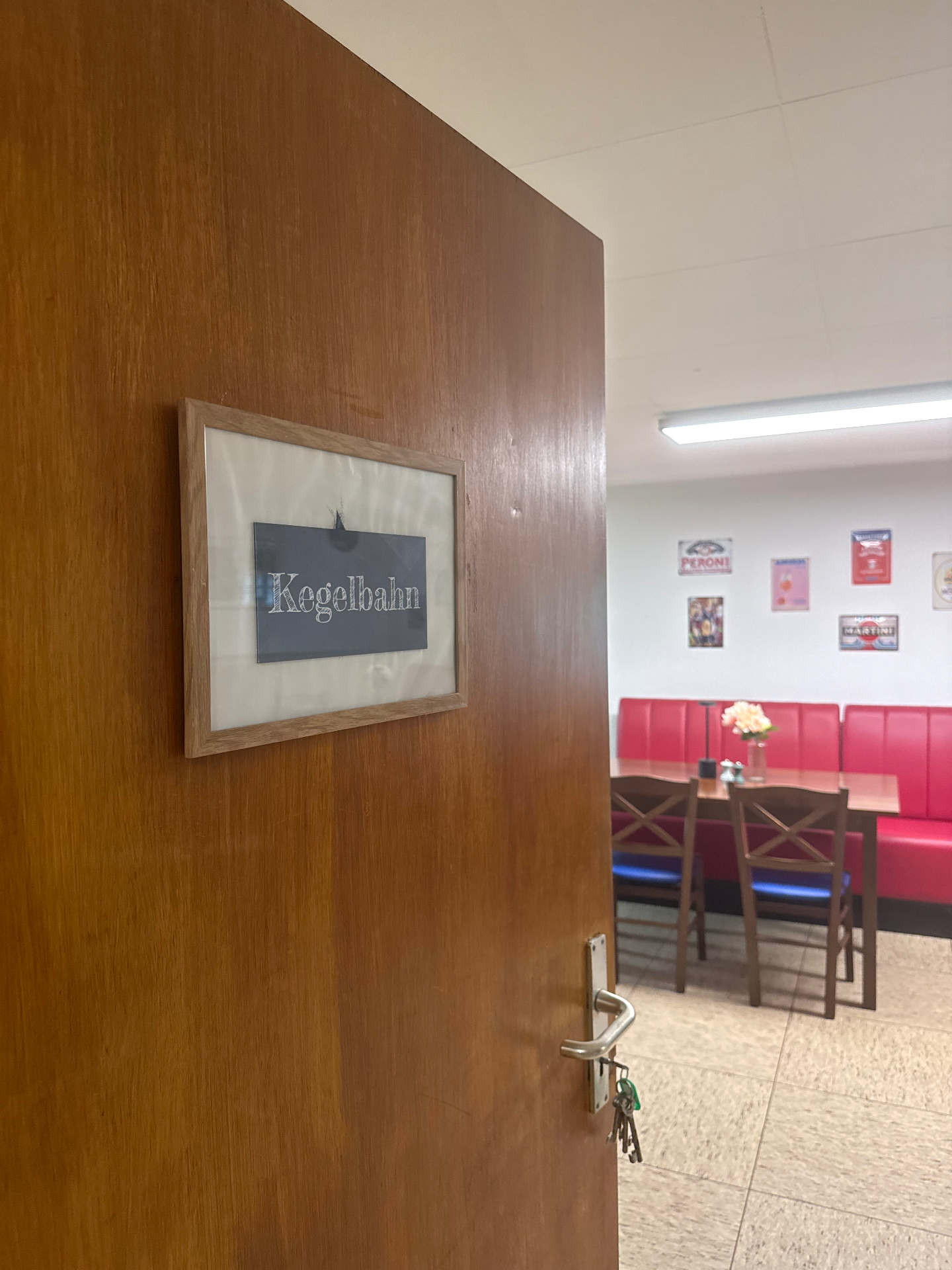 Eingang zur Kegelbahn von La Bottega Wetter: Blick durch die geöffnete Tür mit Kegelbahn-Schild in den separaten Gastraum mit roter Sitzbank